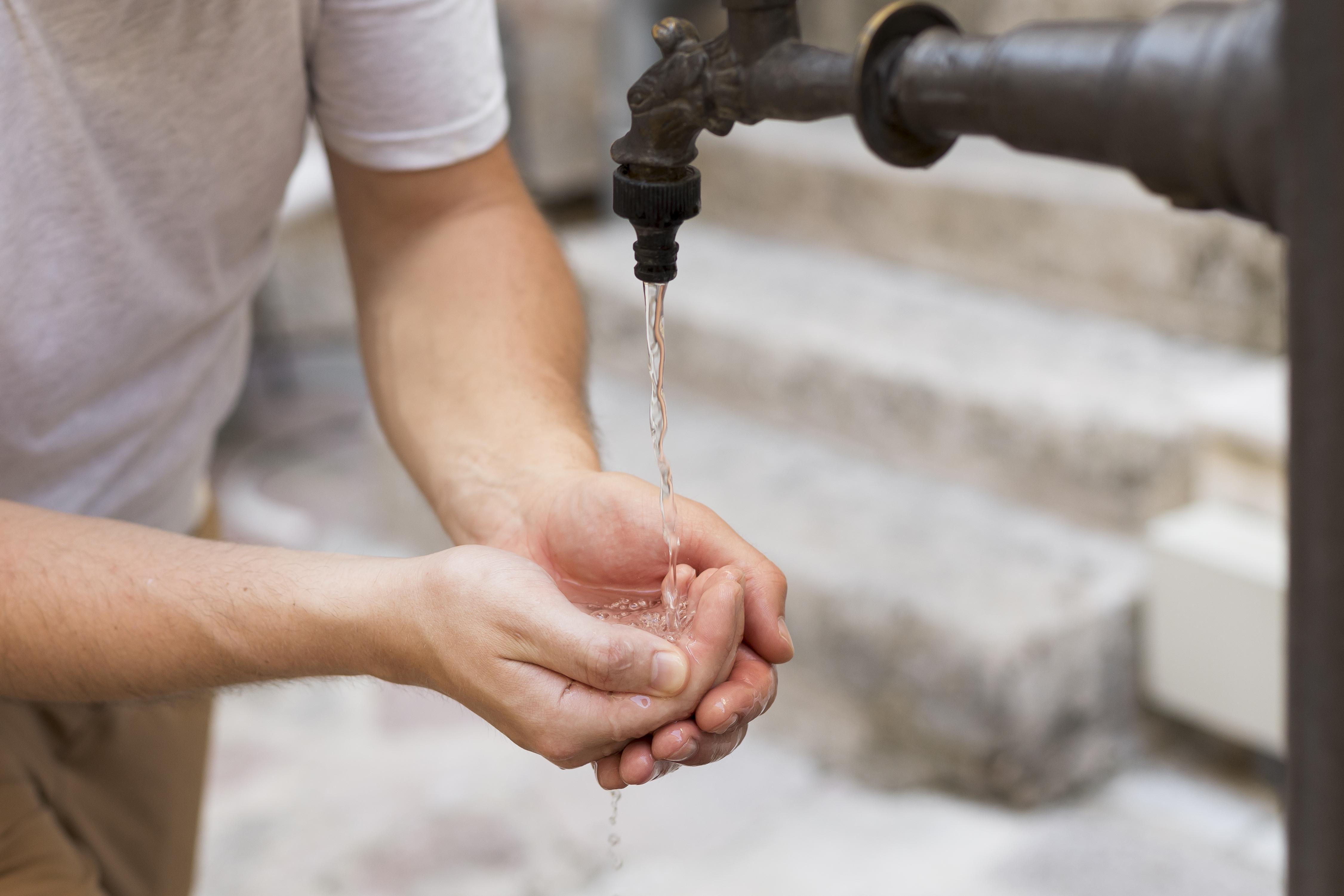 A person washing their hands using an outdoor water source